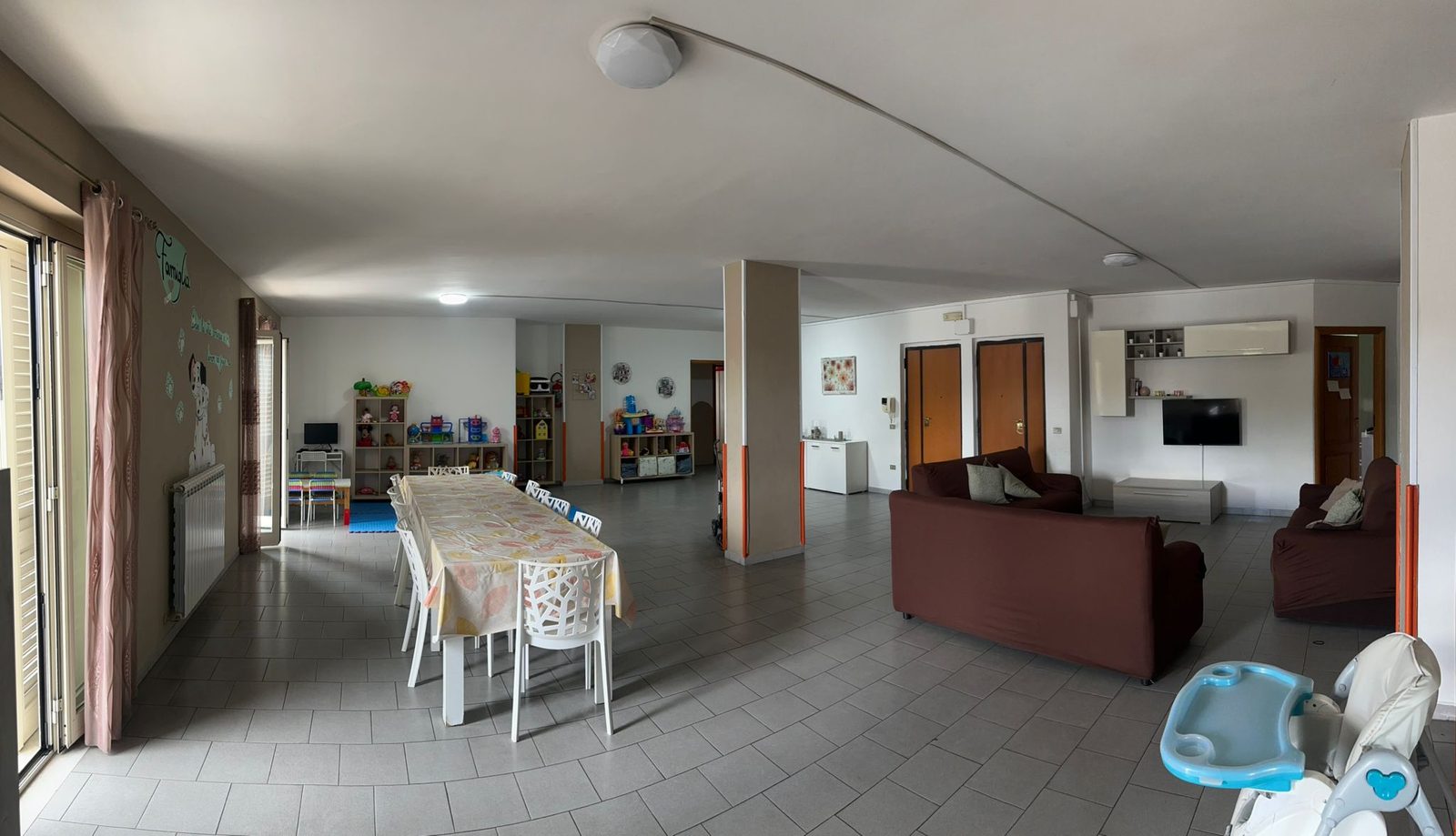 Salone comune con zona pranzo, angolo giochi per bambini e divani nella comunità Casa Mia
